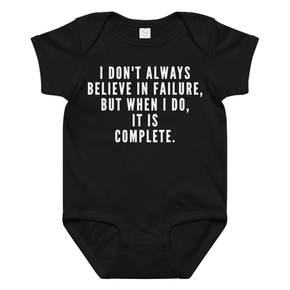 "I don't always believe in failure, but when I do, it is complete." printed on a black baby jersey bodysuit laying on a flat surface amongst other clothes