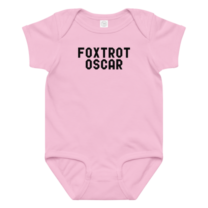 "Foxtrot Oscar" printed on a pink baby jersey bodysuit laying on a flat surface amongst other clothes