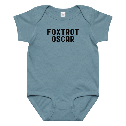 "Foxtrot Oscar" printed on a vintage indigo baby jersey bodysuit laying on a flat surface amongst other clothes
