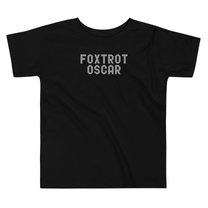 "Foxtrot Oscar" printed on a black toddler short sleeve tee laying on a flat surface