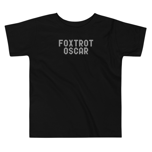 "Foxtrot Oscar" printed on a black toddler short sleeve tee laying on a flat surface