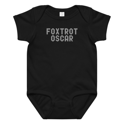 "Foxtrot Oscar" printed on a black baby jersey bodysuit laying on a flat surface amongst other clothes