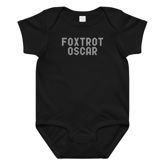 "Foxtrot Oscar" printed on a black baby jersey bodysuit laying on a flat surface amongst other clothes