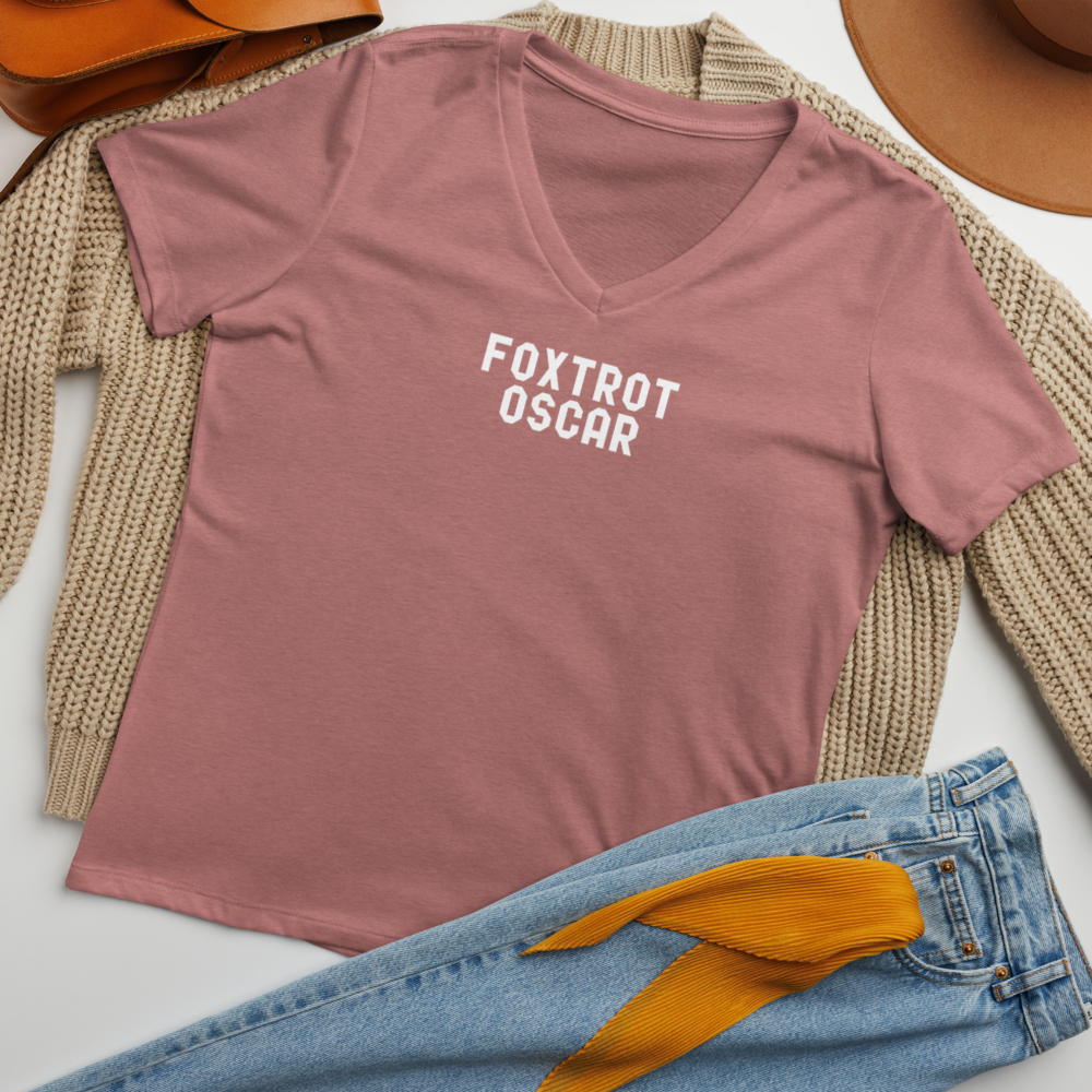 "Foxtrot Oscar" printed on a heather mauve women's relaxed v-neck t-shirt laying on a flat surface amongst other clothes