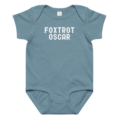 "Foxtrot Oscar" printed on a vintage indigo baby jersey bodysuit laying on a flat surface amongst other clothes