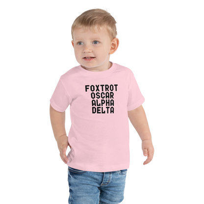 "Foxtrot Oscar Alpha Delta" printed on a pink toddler short sleeve tee worn by a male