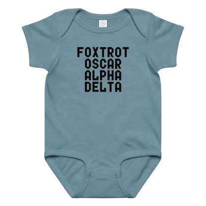 "Foxtrot Oscar Alpha Delta" printed on a vintage indigo baby jersey bodysuit laying on a flat surface amongst other clothes