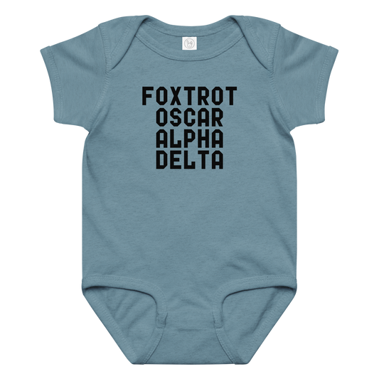 "Foxtrot Oscar Alpha Delta" printed on a vintage indigo baby jersey bodysuit laying on a flat surface amongst other clothes