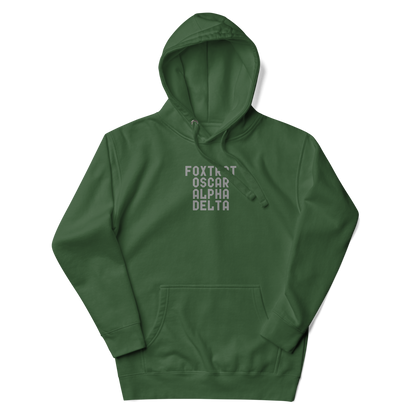 "Foxtrot Oscar Alpha Delta" printed on a forest green unisex hoodie laying on a flat surface with the hood up