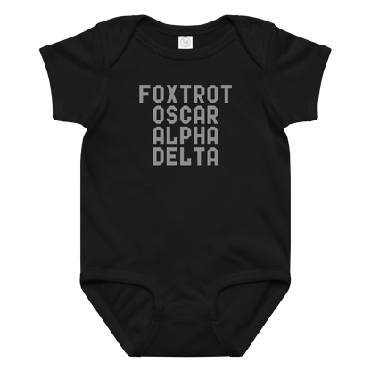 "Foxtrot Oscar Alpha Delta" printed on a black baby jersey bodysuit laying on a flat surface amongst other clothes