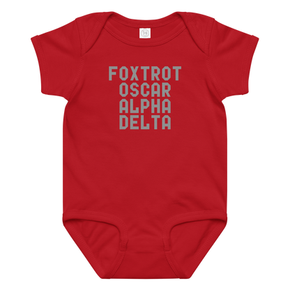 "Foxtrot Oscar Alpha Delta" printed on a red baby jersey bodysuit laying on a flat surface amongst other clothes