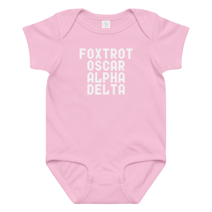 "Foxtrot Oscar Alpha Delta" printed on a pink baby jersey bodysuit laying on a flat surface amongst other clothes