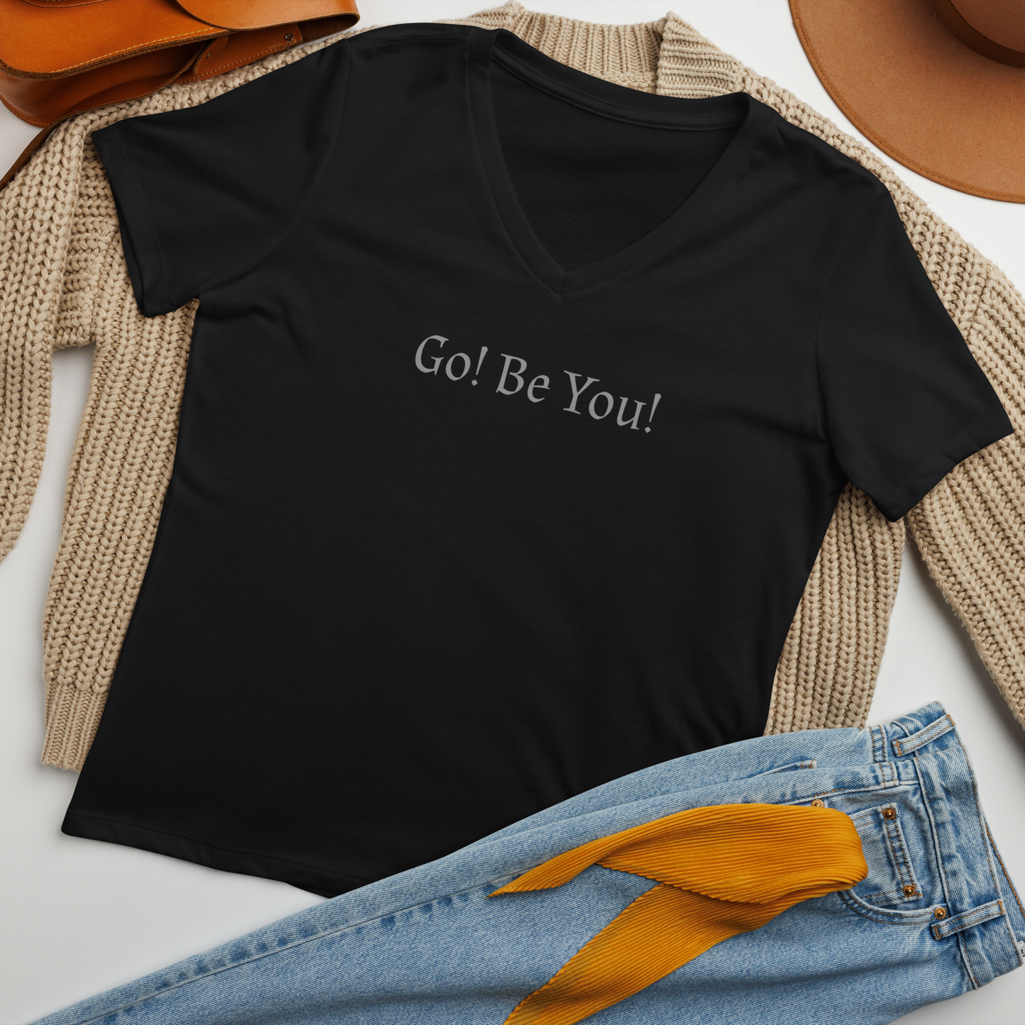 "Go! Be You!" printed on a solid black blend women's relaxed v-neck t-shirt laying on a flat surface amongst other clothes