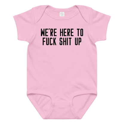 "We're Here To Fuck Shit Up" printed on a pink baby jersey bodysuit laying on a flat surface amongst other clothes
