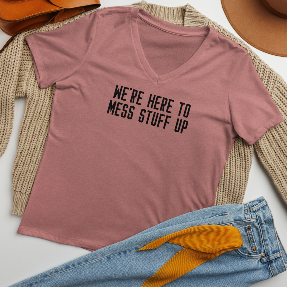 "We're Here To Mess Stuff Up" printed on a heather mauve women's relaxed v-neck t-shirt laying on a flat surface amongst other clothes