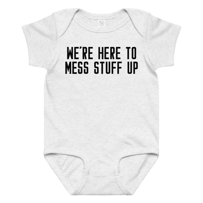"We're Here To Mess Stuff Up" printed on a ash baby jersey bodysuit laying on a flat surface amongst other clothes