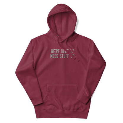 "We're Here To Mess Stuff Up" printed on a maroon unisex hoodie laying on a flat surface with the hood up