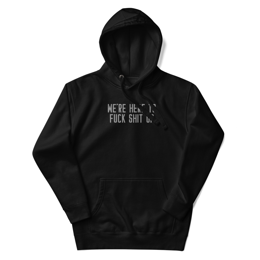 "We're Here To Fuck Shit Up" printed on a black unisex hoodie laying on a flat surface with the hood up