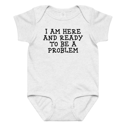 "I am here and ready to be a problem" printed on a ash baby jersey bodysuit laying on a flat surface amongst other clothes