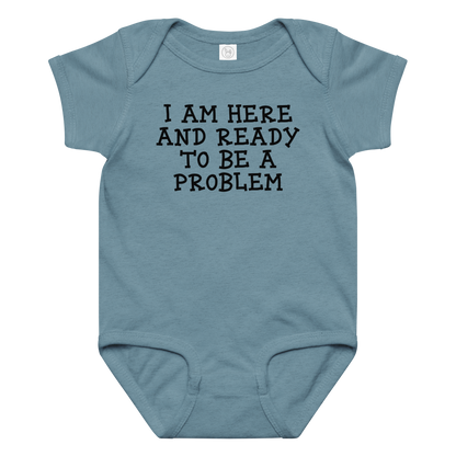 "I am here and ready to be a problem" printed on a vintage indigo baby jersey bodysuit laying on a flat surface amongst other clothes