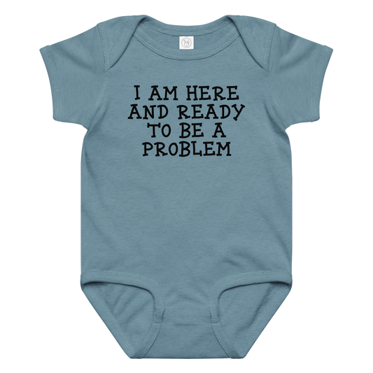 "I am here and ready to be a problem" printed on a vintage indigo baby jersey bodysuit laying on a flat surface amongst other clothes