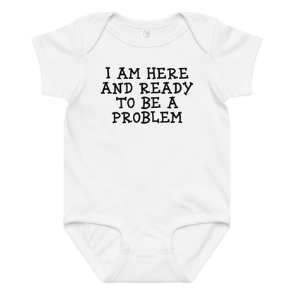 "I am here and ready to be a problem" printed on a white baby jersey bodysuit laying on a flat surface amongst other clothes