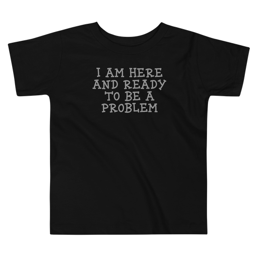 "I am here and ready to be a problem" printed on a black toddler short sleeve tee laying on a flat surface