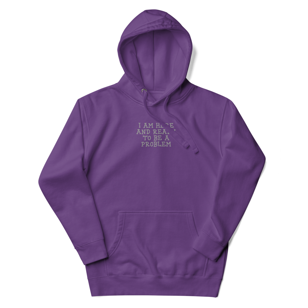 "I am here and ready to be a problem" printed on a purple unisex hoodie laying on a flat surface with the hood up