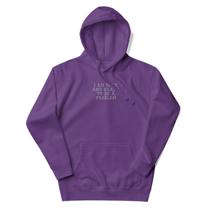 "I am here and ready to be a problem" printed on a purple unisex hoodie laying on a flat surface with the hood up