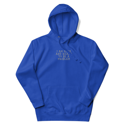 "I am here and ready to be a problem" printed on a team royal unisex hoodie laying on a flat surface with the hood up