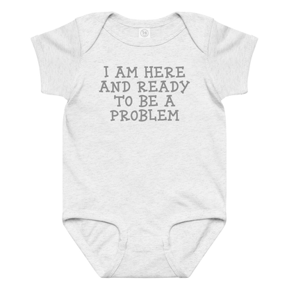 "I am here and ready to be a problem" printed on a ash baby jersey bodysuit laying on a flat surface amongst other clothes