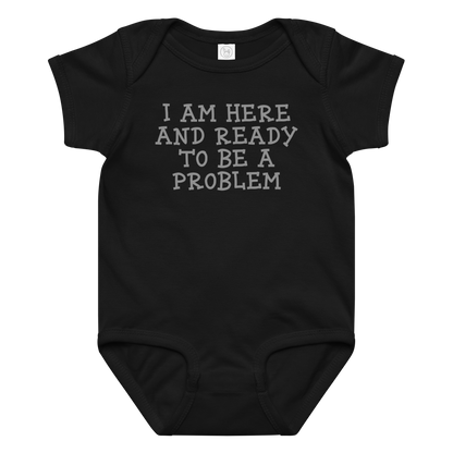 "I am here and ready to be a problem" printed on a black baby jersey bodysuit laying on a flat surface amongst other clothes