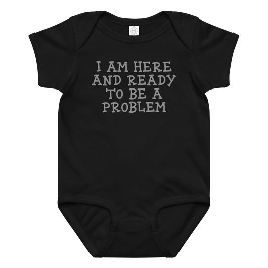 "I am here and ready to be a problem" printed on a black baby jersey bodysuit laying on a flat surface amongst other clothes