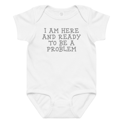 "I am here and ready to be a problem" printed on a white baby jersey bodysuit laying on a flat surface amongst other clothes