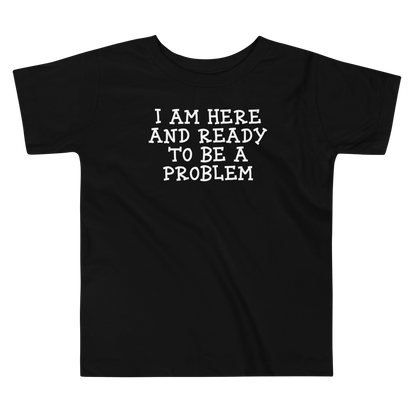"I am here and ready to be a problem" printed on a black toddler short sleeve tee laying on a flat surface