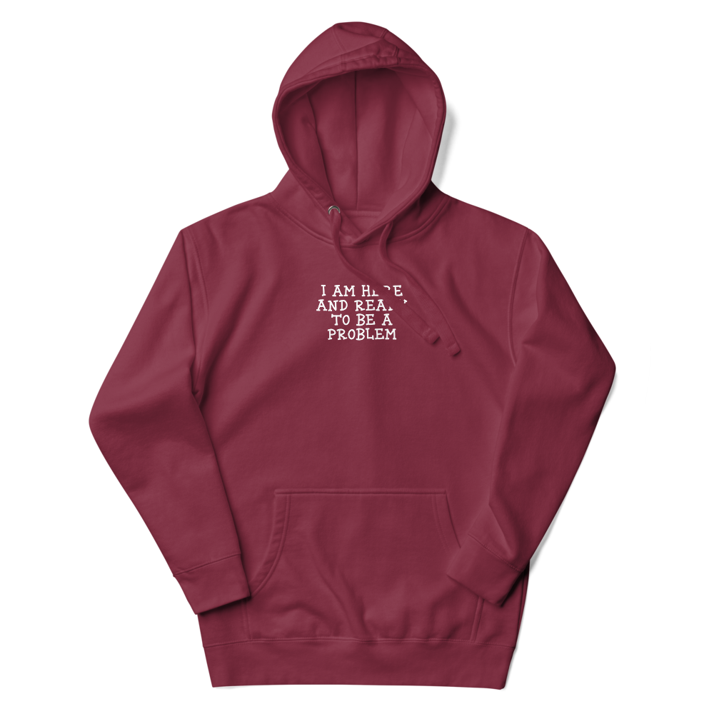 "I am here and ready to be a problem" printed on a maroon unisex hoodie laying on a flat surface with the hood up