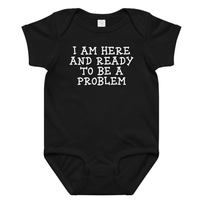 "I am here and ready to be a problem" printed on a black baby jersey bodysuit laying on a flat surface amongst other clothes