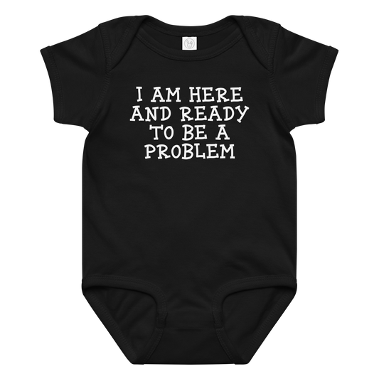 "I am here and ready to be a problem" printed on a black baby jersey bodysuit laying on a flat surface amongst other clothes