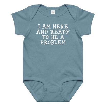 "I am here and ready to be a problem" printed on a vintage indigo baby jersey bodysuit laying on a flat surface amongst other clothes