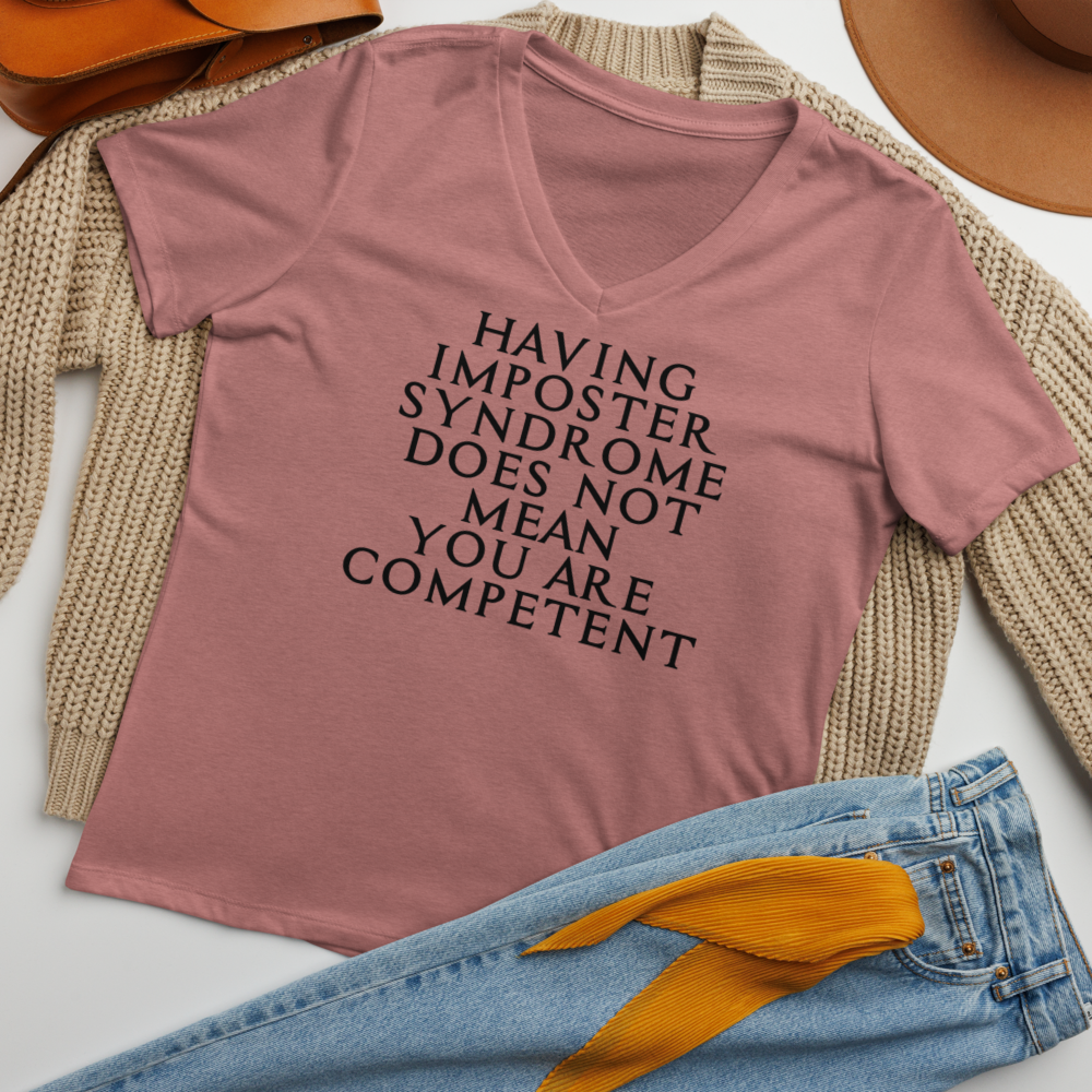 "Having Imposter Syndrome does not mean you are competent" printed on a heather mauve women's relaxed v-neck t-shirt laying on a flat surface amongst other clothes