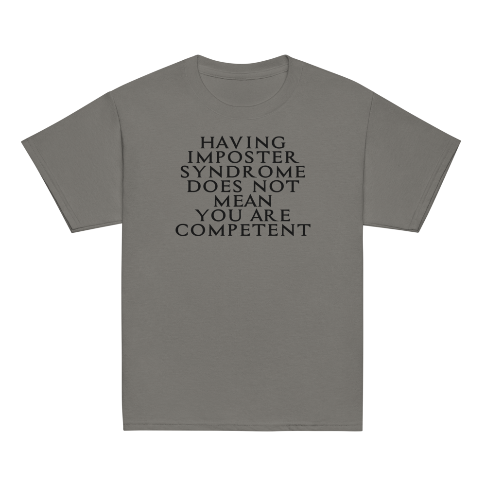"Having Imposter Syndrome does not mean you are competent" printed on a charcoal youth classic tee laying on a flat surface