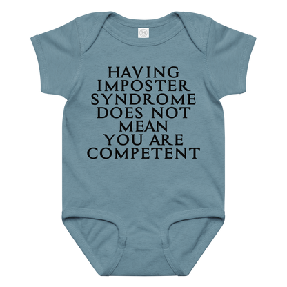 "Having Imposter Syndrome does not mean you are competent" printed on a vintage indigo baby jersey bodysuit laying on a flat surface amongst other clothes