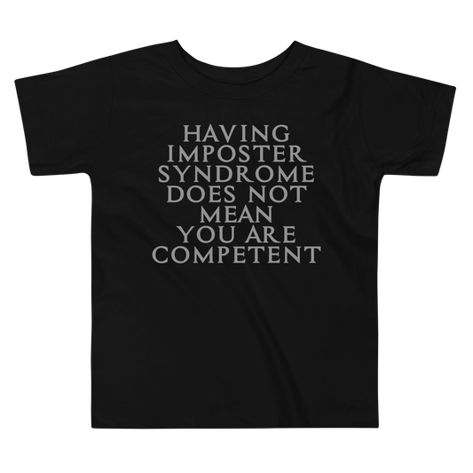 "Having Imposter Syndrome does not mean you are competent" printed on a black toddler short sleeve tee laying on a flat surface