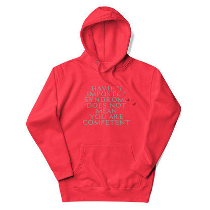 "Having Imposter Syndrome does not mean you are competent" printed on a team red unisex hoodie laying on a flat surface with the hood up