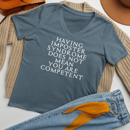 "Having Imposter Syndrome does not mean you are competent" printed on a heather slate women's relaxed v-neck t-shirt laying on a flat surface amongst other clothes