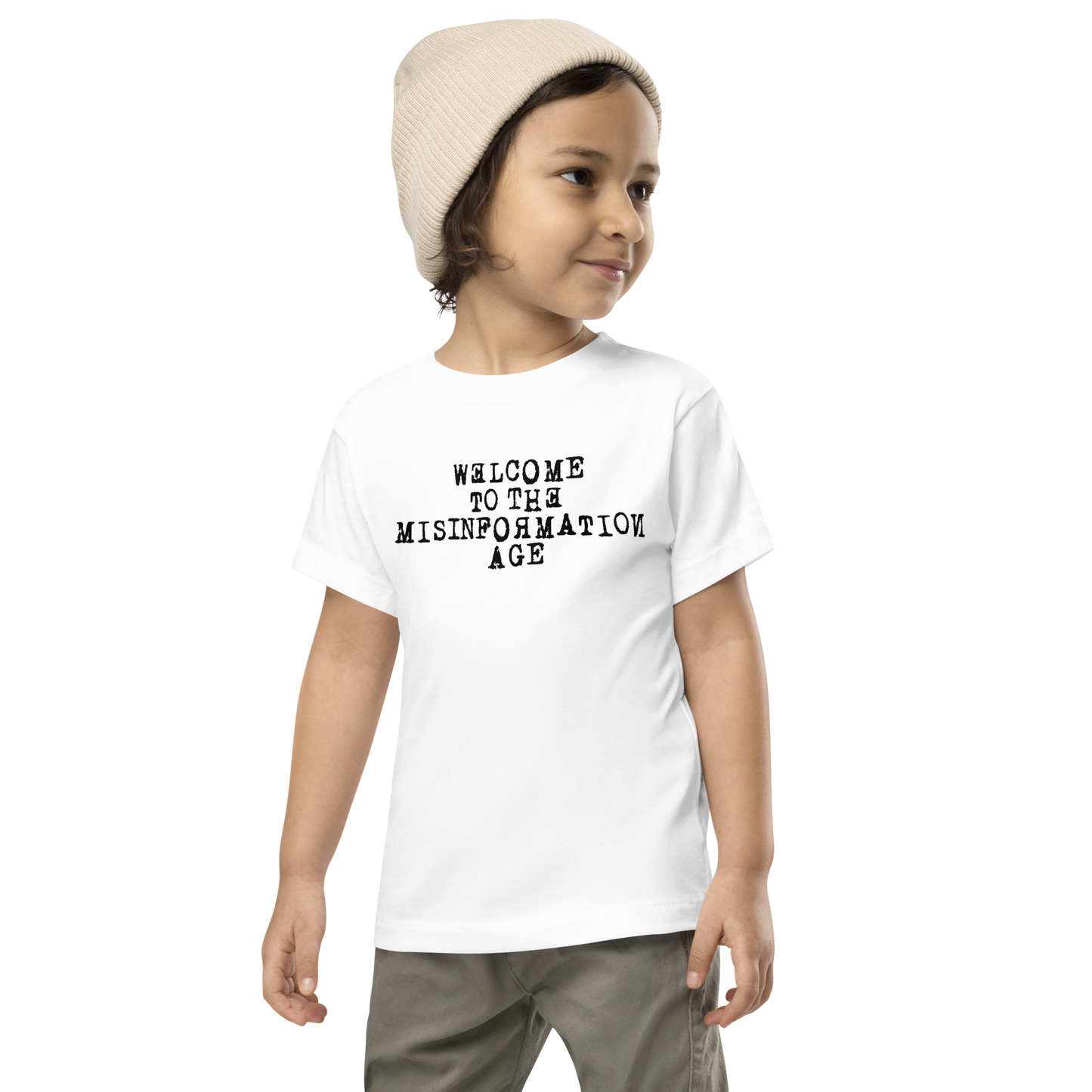 "Welcome to the misinformation age" printed on a white toddler short sleeve tee worn by a male wearing a cap