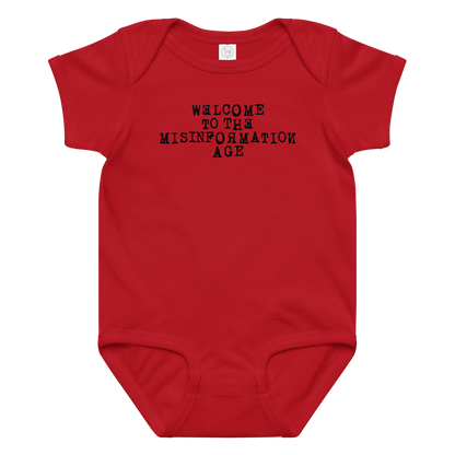 "Welcome to the misinformation age" printed on a red baby jersey bodysuit laying on a flat surface amongst other clothes