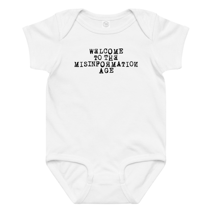 "Welcome to the misinformation age" printed on a white baby jersey bodysuit laying on a flat surface amongst other clothes