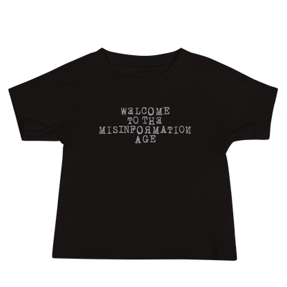 "Welcome to the misinformation age" printed on a black baby jersey short sleeve tee laying on a flat surface