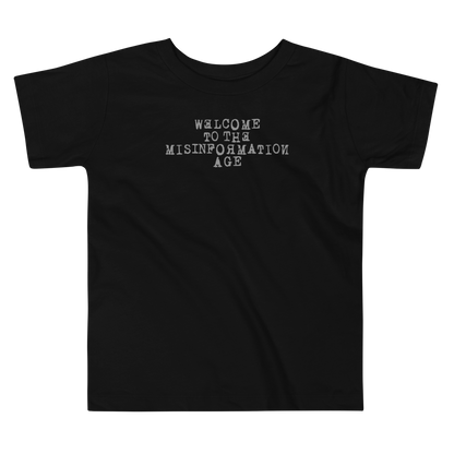 "Welcome to the misinformation age" printed on a black toddler short sleeve tee laying on a flat surface